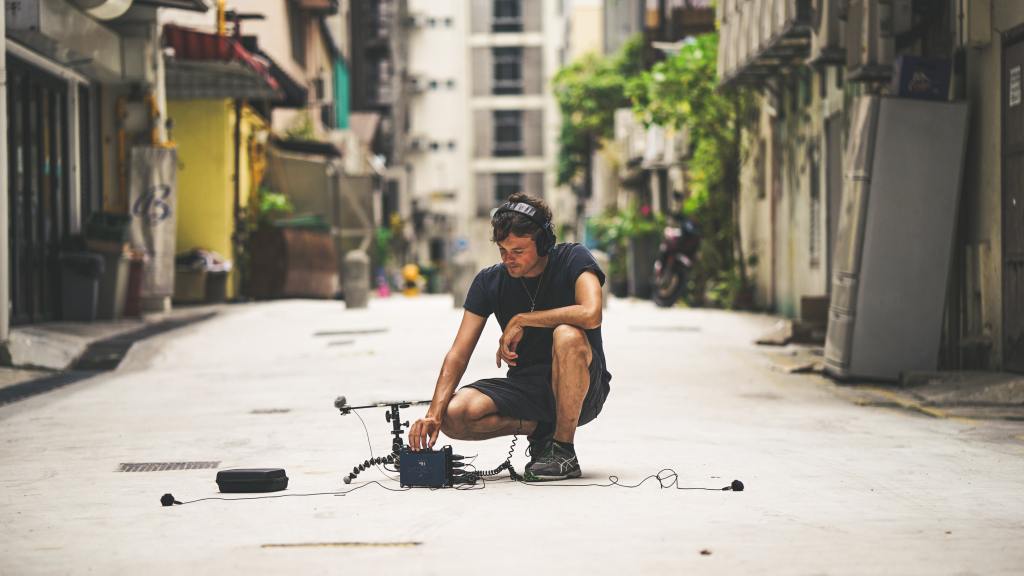 Person crouched in the street recording ambient sounds.