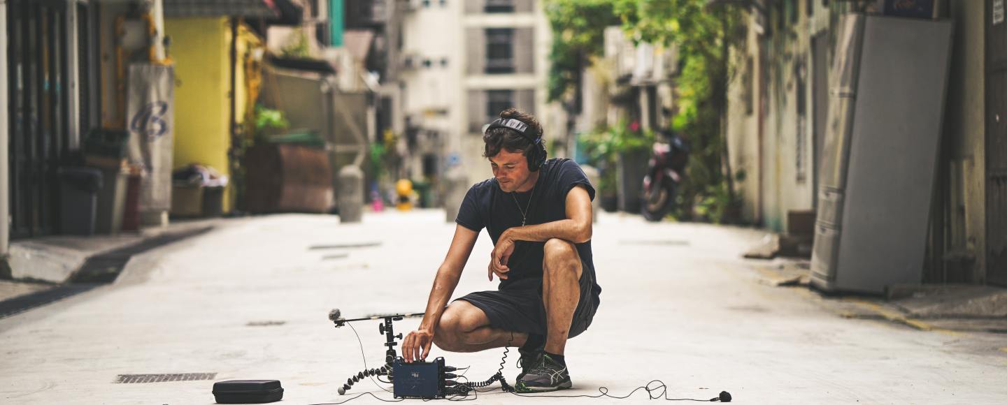Person crouched in the street recording ambient sounds.